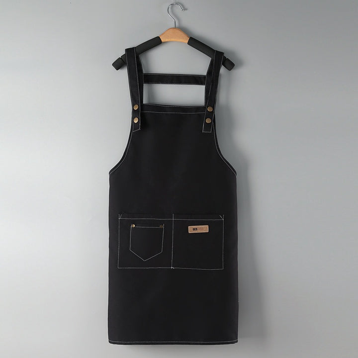 Beauty Salon Apron in black, bib apron with front pockets, on a hanger