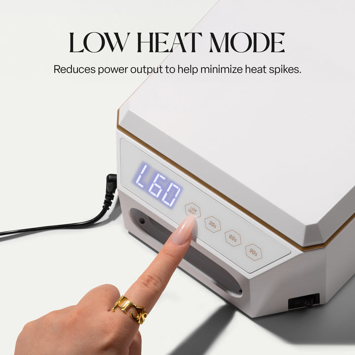 Finger pressing the LOW HEAT button on the Aprés Mini Nova white LED lamp, display showing L60